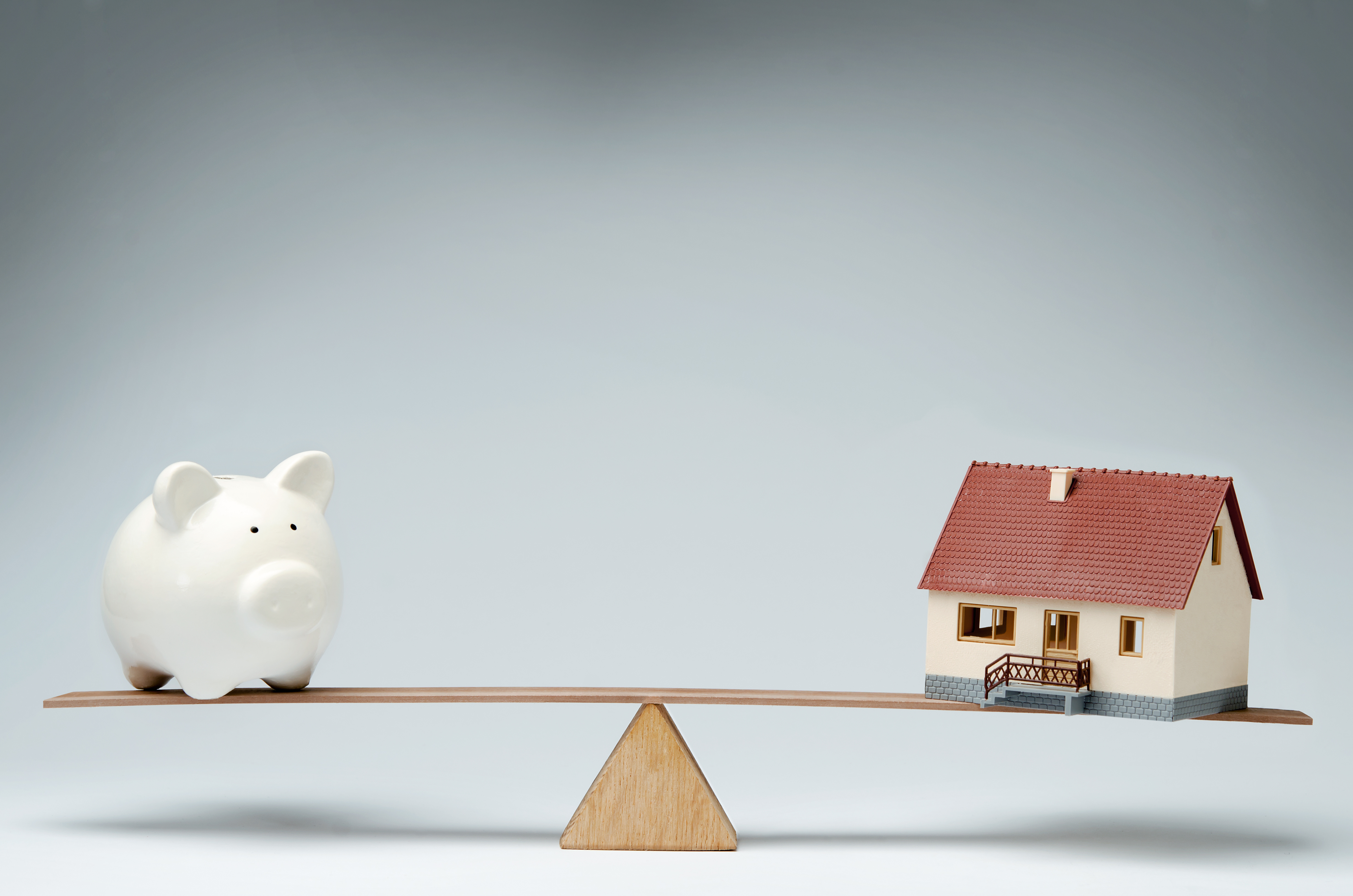 Model house and piggy bank balancing on a seesaw